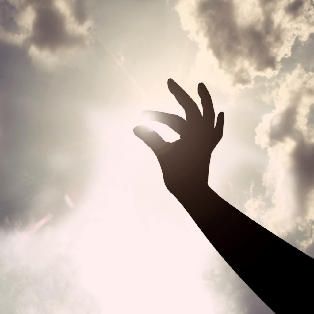 Eine Hand greift gegen das Sonnenlicht in einen bewölkten Himmel